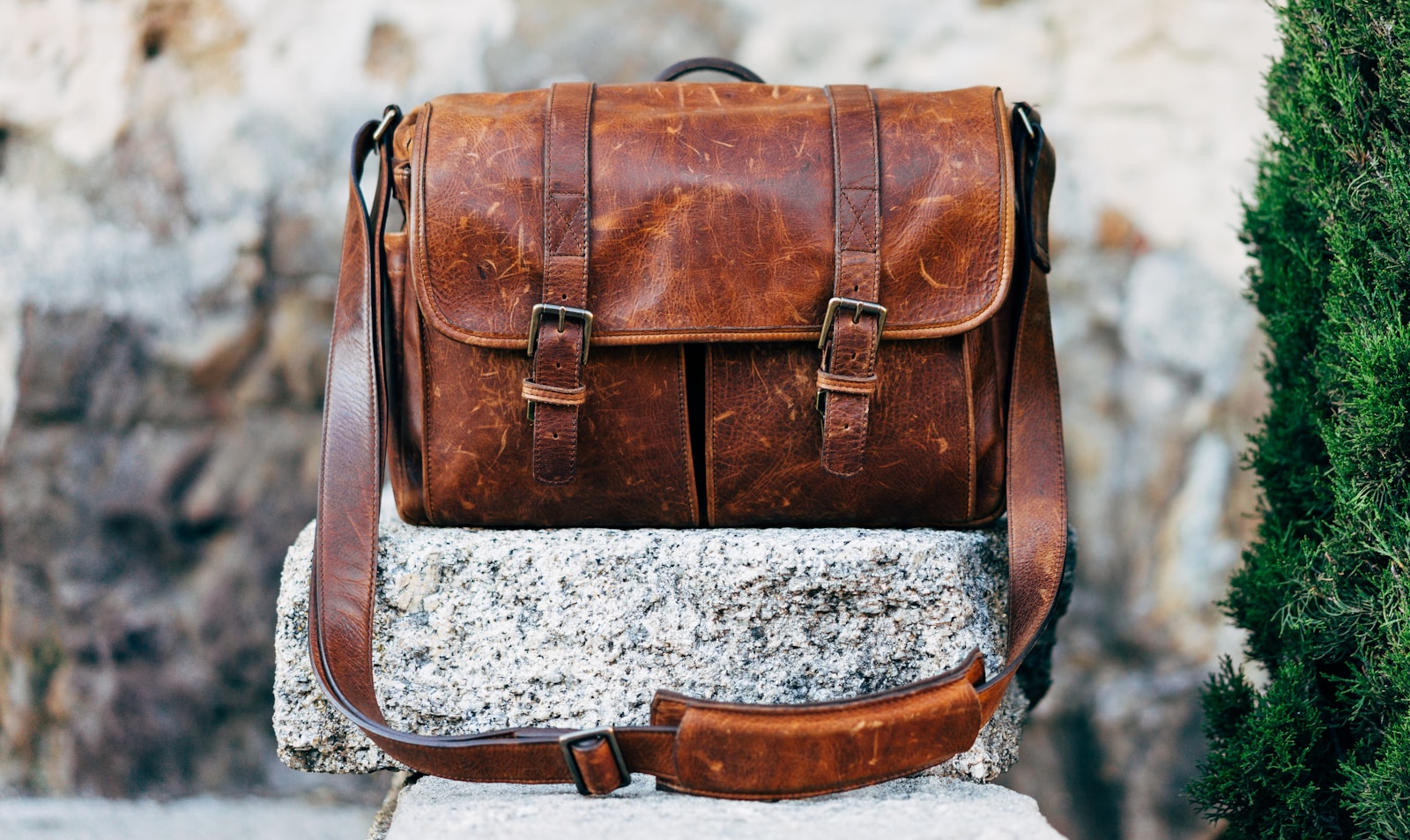 A brown full-grain leather satchel with a crossbody strap, representing the shoulder bags category.